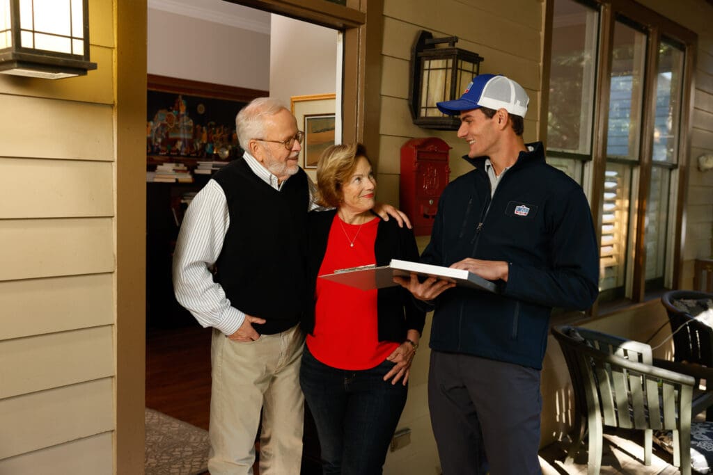 UAT technician speaking with two homeowners on their front porch, in front of open front door.