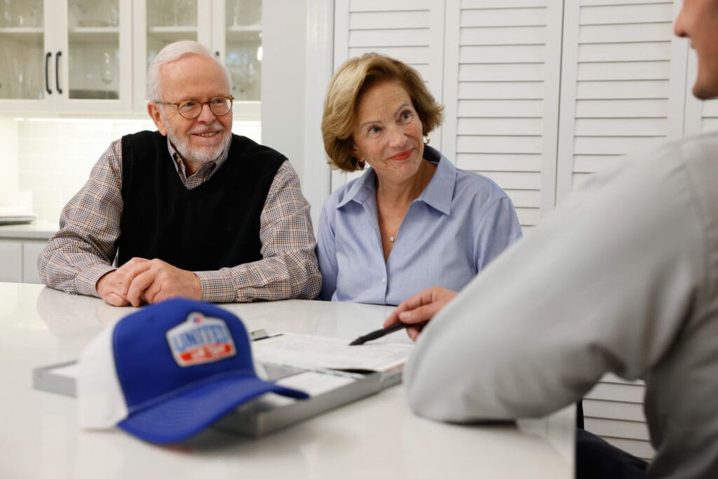 Two homeowners speaking with UAT technician while sitting at a kitchen island with white stone countertop, white cabinets behind them.