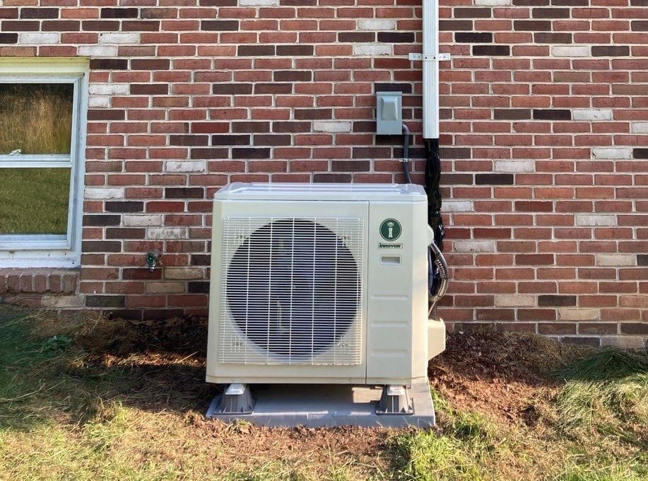 An outdoor heat pump unit installed next to a brick home.