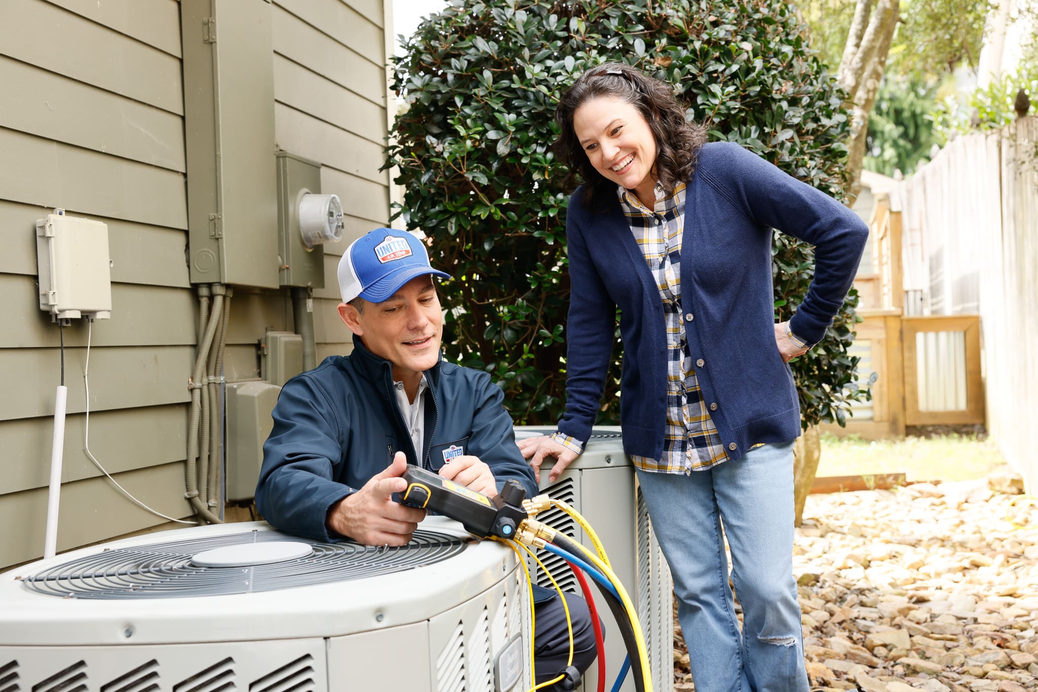 HVAC technician servicing AC unit while talking to a homeowner