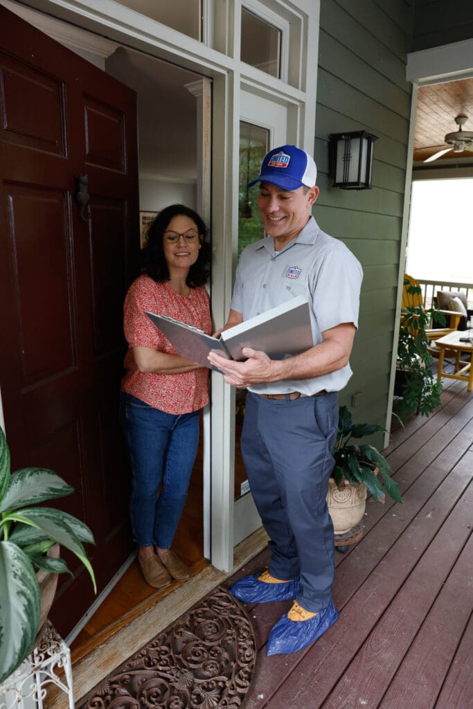 Technician speaking with homeowner at open front door. Technician wearing blue cloth booties over his shoes.