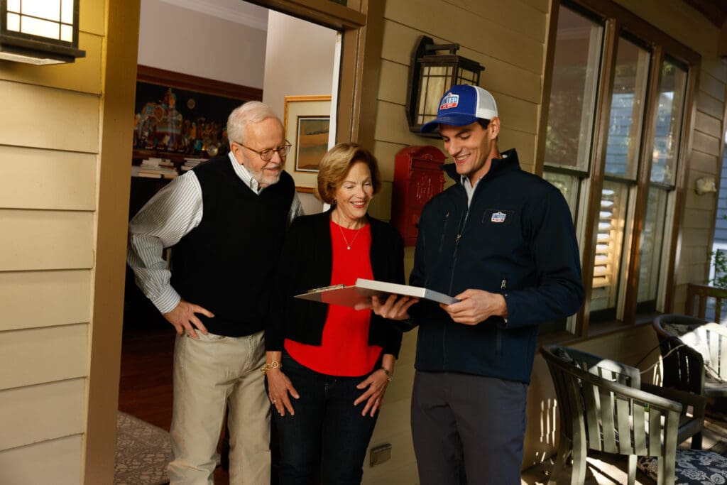 Technician standing next to homeowners in their home, explaining services outlined on clipboard.