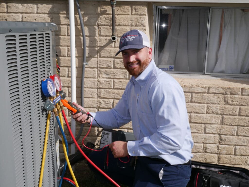 HVAC technician checking refrigerant levels on a unit outside a white brick home.
