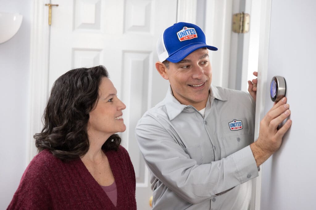UAT technician showing homeowner how to use her smart thermostat on a white wall.