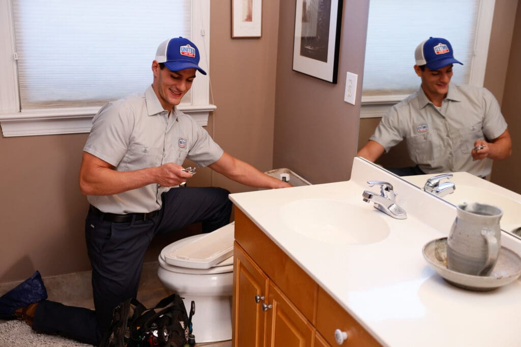 Technician replacing a part in a toilet tank in a home's bathroom.